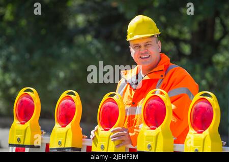 Ein Arbeiter überwacht die Baustellenabsperrung, Mann, 35, 40, Jahre, gelber Schutzhelm, Schutzkleidung, Warnweste, Stockfoto