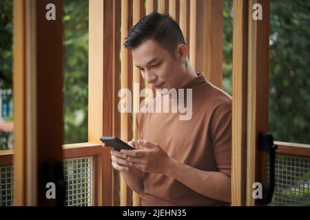 Asiatischer junger Mann doomscrolling, lesen kontinuierlich schlechte Nachrichten auf dem Smartphone Stockfoto