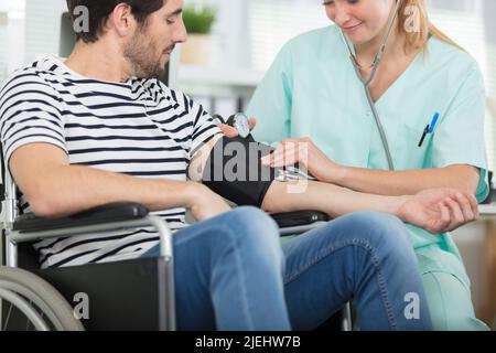 Junge attraktive Krankenschwester, die die Hypertonie des Patienten überprüft Stockfoto