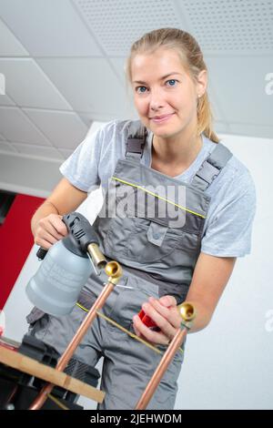 Arbeiterin, die Kupferrohr mit Blasbrenner erhitzt Stockfoto
