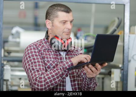 Leitender Ingenieur, der in einer Fabrik einen Laptop verwendet Stockfoto