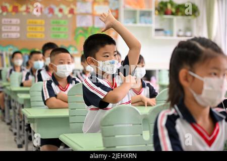 Peking, China. 27.. Juni 2022. Ein Junge hebt seine Hand, um eine Frage an der Yuquan-Schule zu beantworten, die an der Capital Normal University in Peking, der Hauptstadt Chinas, angeschlossen ist, 27. Juni 2022. Pekings Schüler der Grund- und Mittelschule kehrten am Montag nach mehr als 50 Tagen Fernunterricht aufgrund eines Wiederauflebens des COVID-19 auf den Campus zurück. Die Schüler der ersten beiden Jahre der höheren und höheren Mittelschulen oder der Klassen 7, 8, 10 und 11 sowie der Grundschulen nahmen den persönlichen Unterricht wieder auf. Die Ausbildung für Studenten der Klassen 9 und 12 wurde früher abgeschlossen. Kredit: Li Xin/Xinhua/Alamy Live Nachrichten Stockfoto