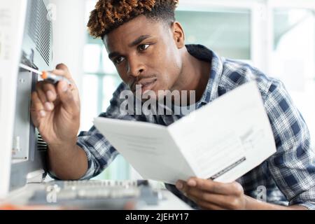 Der junge Mann verwendet einen Schraubendreher, um den Drucker zu reparieren Stockfoto