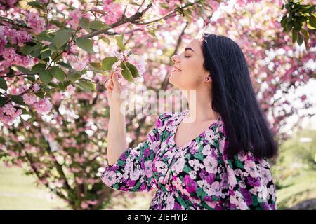 Schwangerin in einem Kleid mit schwarzem Haar in der Nähe von Kirschblüten im Frühjahr Stockfoto