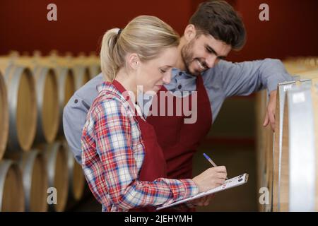 Lächelnde Profis füllen Papierkram im Weinkeller aus Stockfoto