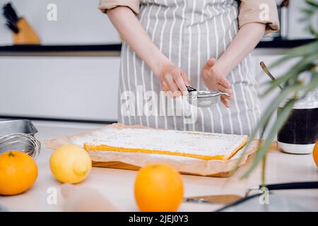 Köche Hände mit kleinem Sieb zum Backen. Baker dekorieren und bestreuen Orangenkuchen oder Kuchen mit Puderzucker. Küche Hintergrund, hausgemacht und Hand Stockfoto