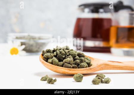 Frischer Oolong-Tee mit Ginseng. Ein Stapel gerollter Tees in einem Holzlöffel. Teesortiment im Geschäft. Chinesischer oder orientalischer gesunder, koffeinhaler Tee. Glastee Stockfoto