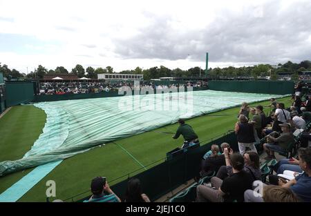 Die Bodenmitarbeiter bringen die Abdeckungen des Platzes wegen Regen am Tag einer der Wimbledon Championships 2022 im All England Lawn Tennis and Croquet Club, Wimbledon. Bilddatum: Montag, 27. Juni 2022. Stockfoto