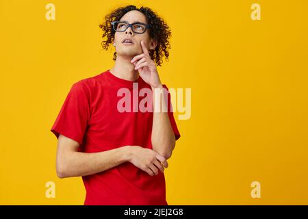 Nachdenklich nachdenkliche myopische junge Student Mann in roten T-Shirt lustige Brille posiert isoliert auf über gelben Studio-Hintergrund. Das beste Angebot mit gratis Stockfoto