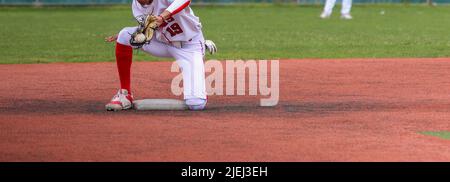 Ein High School Baseballspieler spielt auf dem Spielfeld, indem er den Ball während eines Spiels auf einem Rasenfeld über die zweite Basis zurückgibt. Stockfoto