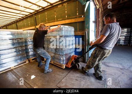 REGION ZAKARPATTIA, UKRAINE - 24. JUNI 2022 - Männer ziehen eine Palette von abgefülltem Wasser aus dem Memory and Roots Zakarpattya Fund in eine Frachtgut Stockfoto