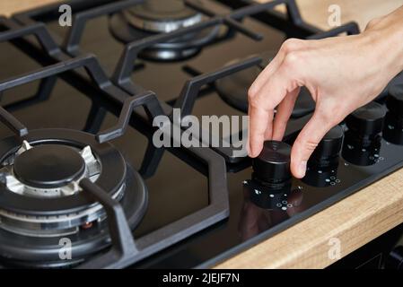 Weibliche Hand, die die Temperatur auf dem Bedienfeld des Gaskochfelds anpasst, Frau, die einen Gasherd verwendet, moderne Haushaltsgeräte Stockfoto