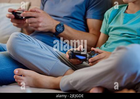 Sonne und Vater spielen Videospiele zu Hause, Familie verbringt Zeit zusammen, glückliche Beziehung, Online-Unterhaltung und Freizeitaktivitäten, Stockfoto
