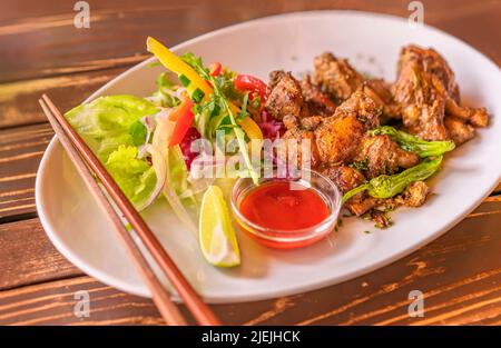 Jamaikanischer Jerkhuhnteller mit Gemüse wie Salada, Scheiben gelber und roter Paprika, Zitrone auf einem Teller mit Essstäbchen in einem japanischen Restaurant Stockfoto