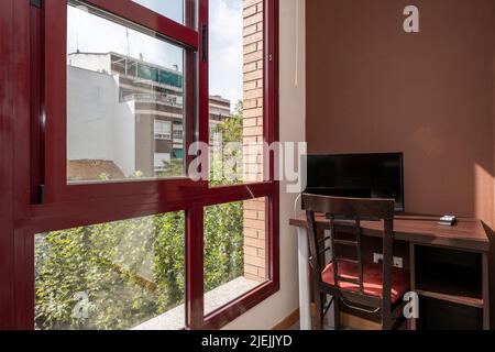 Schreibtisch mit Stuhl und fernseher neben einem Fenster mit roten Aluminiumrahmen Stockfoto