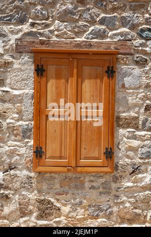 Geschlossene Holzfenster und Fensterläden in der Steinmauer. Holzfenster in einer alten Steinmauer. Stockfoto