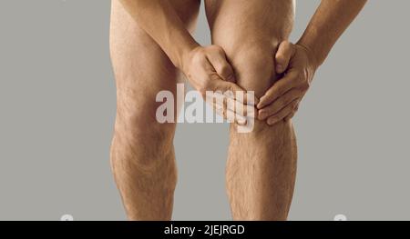 Der junge Mann, der an rheumatoider Arthritis leidet, spürt Schmerzen und berührt sein Knie Stockfoto