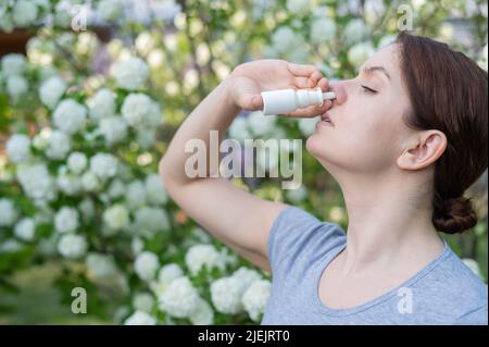 Kaukasische Frau verwendet ein Nasenspray, während sie im Park spazieren geht. Stockfoto