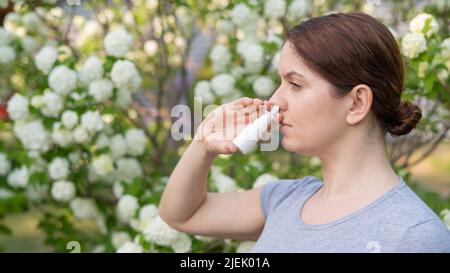 Kaukasische Frau verwendet ein Nasenspray, während sie im Park spazieren geht. Stockfoto