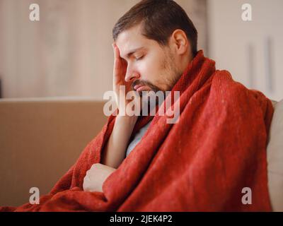 Coronavirus. Kranker Mann mit Corona-Virus, der sich auf dem Sofa niederlegt und sich von einer Krankheit zu Hause erholt. Seine Nase bläst. Das Konzept der hohen Temperaturen. Die Person ist schwer krank. Stockfoto