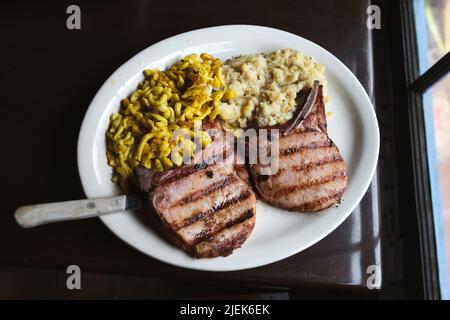 Geräucherte und gegrillte Schweineställe mit einer Seite Käsespätzle und Kartoffelpüree auf einem Teller mit einem großen Messer Stockfoto