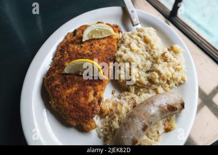 Deutsches Schweineschnitzel mit Sauerkraut, Bratwurst und Kartoffelpüree zum Abendessen auf einem Teller Stockfoto