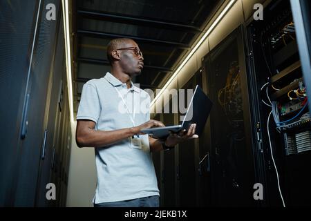 Porträt eines afroamerikanischen Mannes, der das Servernetzwerk verwaltet und einen Laptop und einen IT-Techniker verwendet Stockfoto