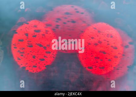 Abstrakte Ansicht der bunten blauen und roten Bokeh Kreise von Verkehrsfarben auf Straßenlicht Hintergrund mit nassen regen Tropfen auf Windschutzscheibe Armaturenbrett von Auto c Stockfoto