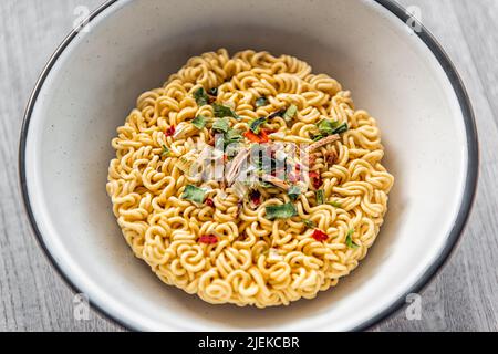 Makro-Nahaufnahme von trockener, würziger roter Ramen-Nudelsuppe in einer Schüssel als japanisches asiatisches Gericht mit Textur aus roher Pasta und grünen Zwiebeln Stockfoto