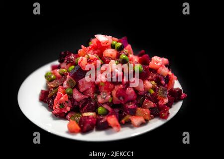 Makro-Nahaufnahme der traditionellen russischen oder ukrainischen Rüben-Salat Vinaigrette Vorspeise auf dem Tisch isoliert schwarzen Hintergrund mit Karotten, grünen Erbsen und Oni Stockfoto