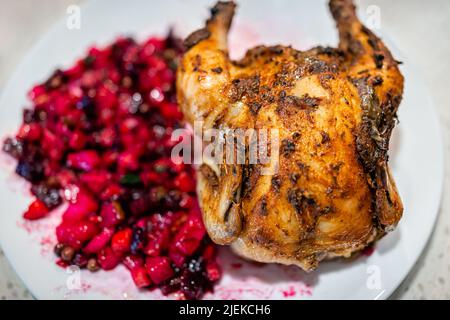 Makro-Nahaufnahme von russischem oder ukrainischem gekochtem Rübenkartoffelsalat namens Vinaigrette auf dem Teller mit einer ganzen gerösteten kornischen Henne und knuspriger Haut Stockfoto