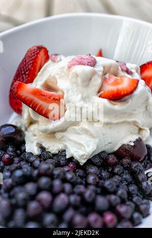Nahaufnahme Makro vertikale Ansicht von Vanilleeis gekrönt mit frisch geschnittenen Scheiben von roten Erdbeerbeeren und blauen Heidelbeeren mit Sakura Kirsche Blosso Stockfoto