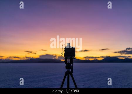 Bonneville Salt Flats in der Nähe von Salt Lake City, Utah bei farbenprächtiger Dämmerung nach Sonnenuntergang mit violettem und gelbem Himmel und Stativ mit Kamera, die Zeitrafferaufnahmen macht Stockfoto