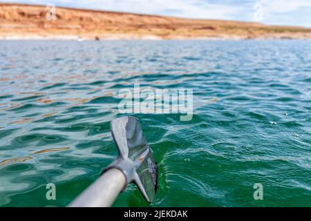 Kajakfahren in Lake Powell in Richtung Antilope Canyon mit Nahaufnahme des Paddelruders durch die blaue Wasseroberfläche und Felsformationen im Hintergrund Stockfoto