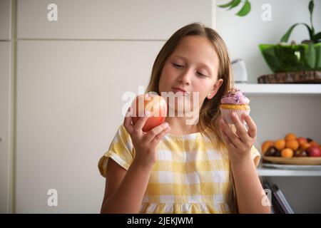 Das Mädchen wählt zwischen einem Cupcake und einem Apfel Stockfoto