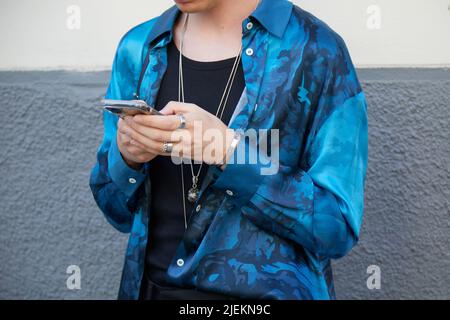 MAILAND, ITALIEN - 18. JUNI 2022: Mann mit blauem Camouflage-Shirt beim Blick auf das Smartphone vor Marcelo Burlon County of Milan Fashion Show, Milan Fashion W Stockfoto