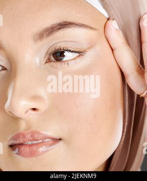 Gesicht einer schönen muslimischen Frau, die ein braunes Kopftuch trägt und die Haut um ihre Augen hebt. Kopfschuss einer Hijab-Dame, die eine Liftschirurgie in Erwägung zieht Stockfoto