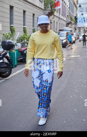 MAILAND, ITALIEN - 18. JUNI 2022: Mann mit blauer Hose mit Blumenmuster und gelbem Pullover vor der Versace Fashion Show, Milan Fashion Week Street Sty Stockfoto