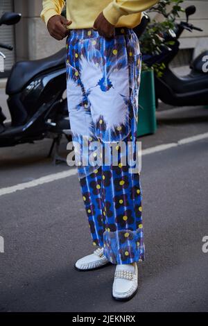 MAILAND, ITALIEN - 18. JUNI 2022: Mann mit blauer Hose mit Blumenmuster und weißen Schuhen mit Perlen vor der Versace Fashion Show, Mailand Fashion Week s Stockfoto