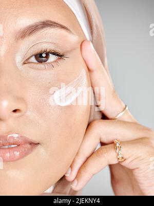 Porträt einer jungen muslimischen Frau, die einen Hijab oder ein Kopftuch trägt und eine Feuchtigkeitscreme auf ihre makellose Haut aufträgt, während sie ihre Wimpern-Extensions zeigt Stockfoto