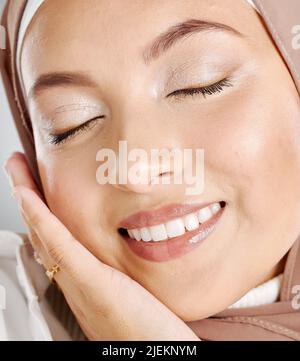 Nahaufnahme einer schönen muslimischen Frau mit geschlossenen Augen, die sich mit ihrer Hautpflegeroutine zufrieden fühlt. Headshot einer atemberaubenden Dame mit glühendem Make-up und Stockfoto