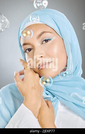 Studioporträt einer schönen jungen muslimischen Frau mit blauem Kopftuch vor grauem Hintergrund mit Blasen. Glückliche arabische Frau trägt Make-up mit Stockfoto