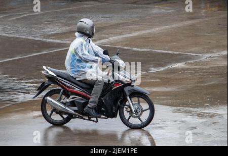 Ein Mann mit Regenmantel fährt im Regen ein Motorrad Stockfoto