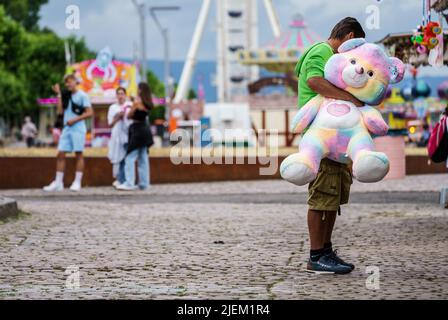 Mainz, Deutschland. 27.. Juni 2022. Ein Mann steht mit einem riesigen ausgestopften Bären auf der Messe, die im Rahmen der Johannisnacht in Mainz am Rheinufer stattfindet. Die Johannisnacht (24,06 - 27.06.22) findet seit 1968 jährlich zu Ehren von Johannes Gutenberg statt. Quelle: Andreas Arnold/dpa/Alamy Live News Stockfoto