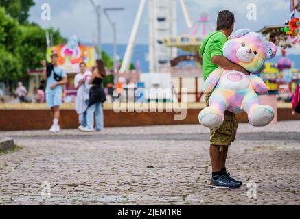 Mainz, Deutschland. 27.. Juni 2022. Ein Mann steht mit einem riesigen ausgestopften Bären auf der Messe, die im Rahmen der Johannisnacht in Mainz am Rheinufer stattfindet. Die Johannisnacht (24,06 - 27.06.22) findet seit 1968 jährlich zu Ehren von Johannes Gutenberg statt. Quelle: Andreas Arnold/dpa/Alamy Live News Stockfoto