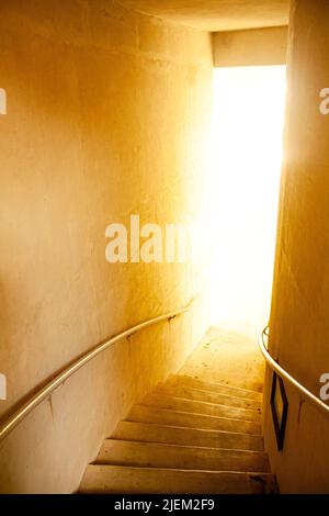 Ein Treppenhaus, das zu einem hellen, warmen Licht führt Stockfoto