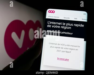 Person, die Smartphone mit der Webseite des belgischen Telekommunikationsunternehmens Voo SA auf dem Bildschirm vor dem Logo hält. Konzentrieren Sie sich auf die Mitte des Telefondisplays. Stockfoto