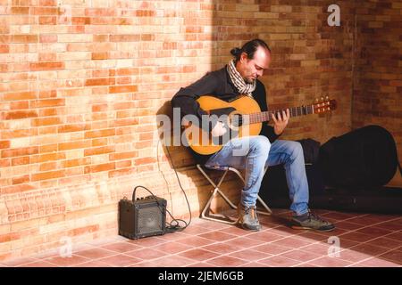 Sevilla, Spanien - 31. Januar 2022: Ein männlicher Straßenmusiker, der spanische Akustikgitarre mit einem kleinen Verstärker spielt Stockfoto