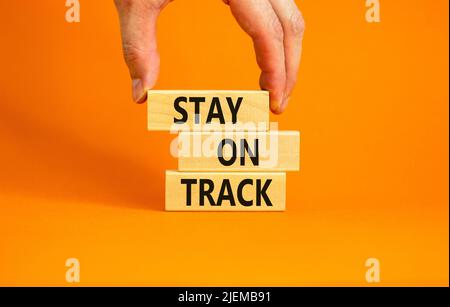 Symbol „auf Kurs bleiben“. Konzeptwörter bleiben auf Holzblöcken auf einem wunderschönen orangen Hintergrund auf Kurs. Geschäftsmann Hand. Business, Motivati Stockfoto