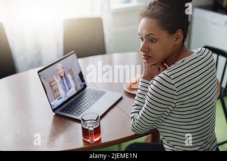 Draufsicht auf eine junge Frau mit gemischter Rasse, die beim Videoanruf am Tisch sitzt Stockfoto